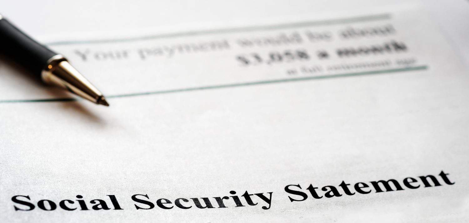 A close-up, slightly angled view of a white paper document titled 'Social Security Statement' at the bottom. A black and gold pen rests across the top part of the document, which shows blurred text including '$3,058 a month' under the heading 'Your payment would be about'.