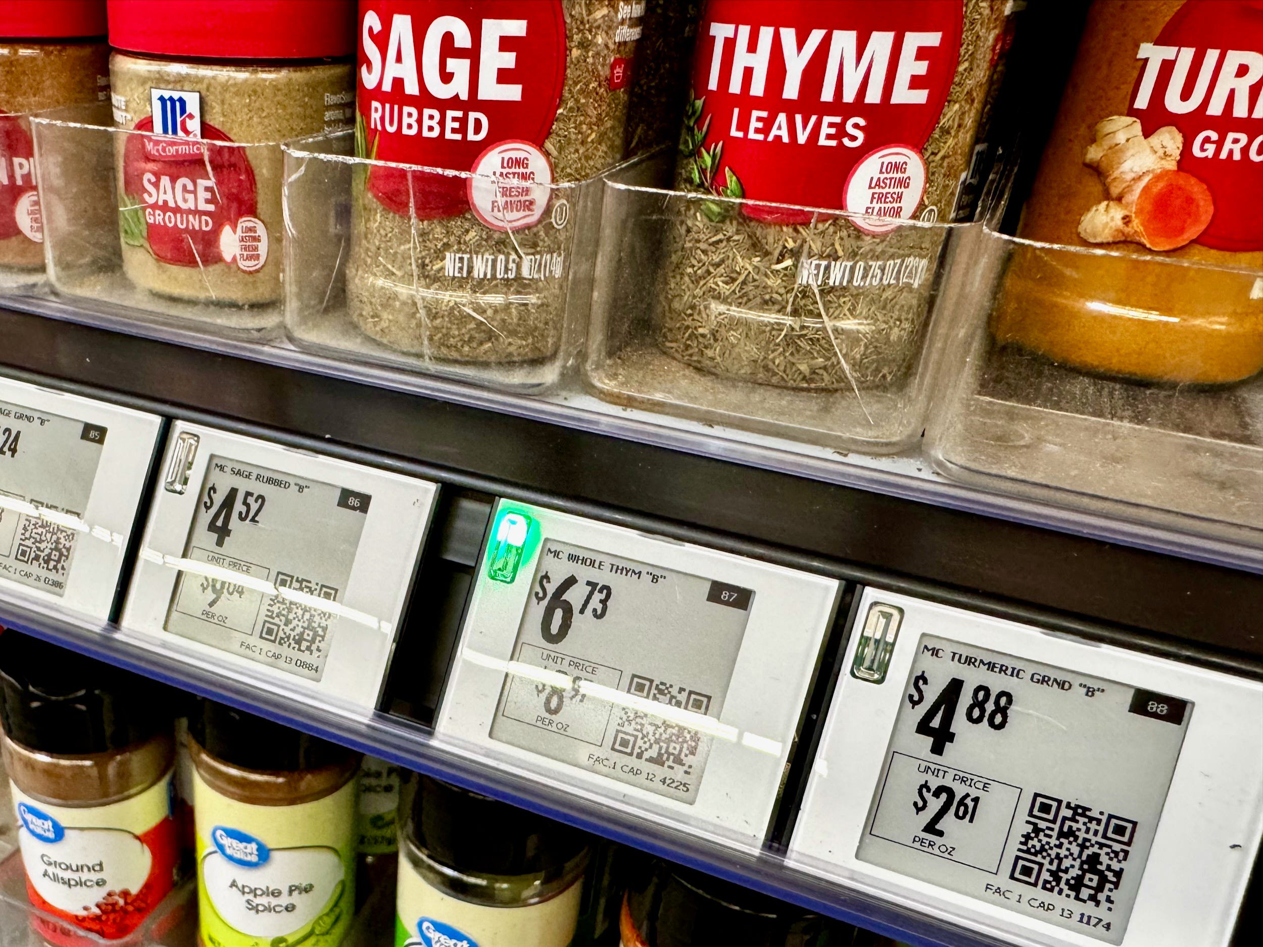 Jars of spices including sage and thyme are displayed with electronic shelf labels showing prices and QR codes.