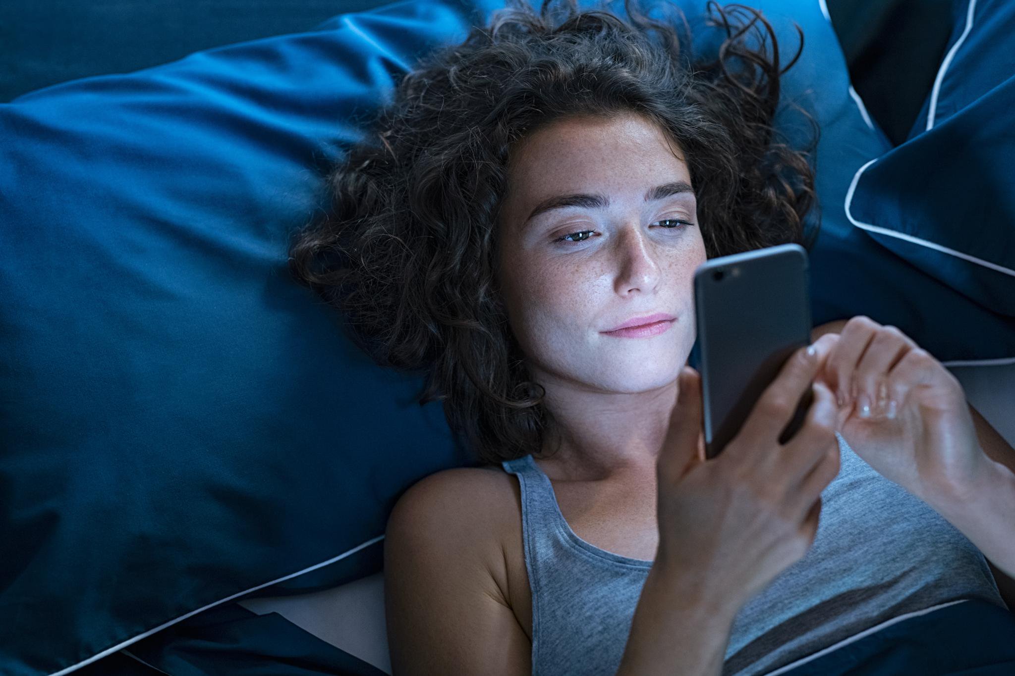 A young woman lying in bed at night, using her smartphone.
