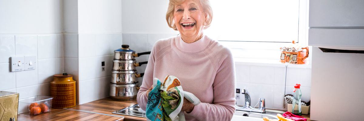 Mature woman holding hand towel and smiling after doing the dishes.
