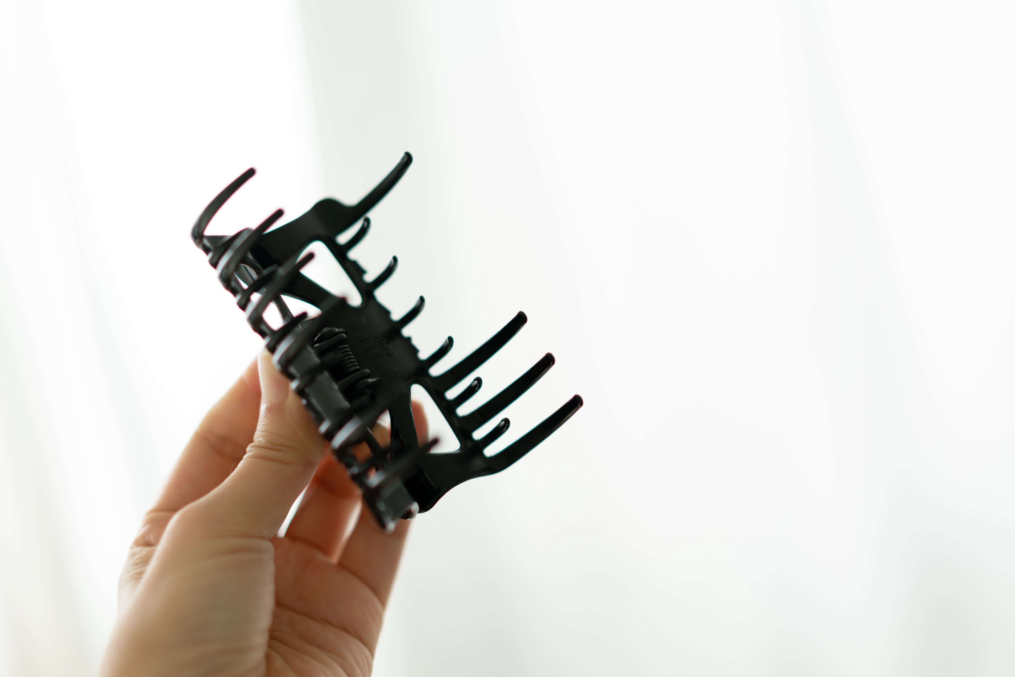 A hand holding a hair claw clip against a plain background, illustrating a health or beauty accessory