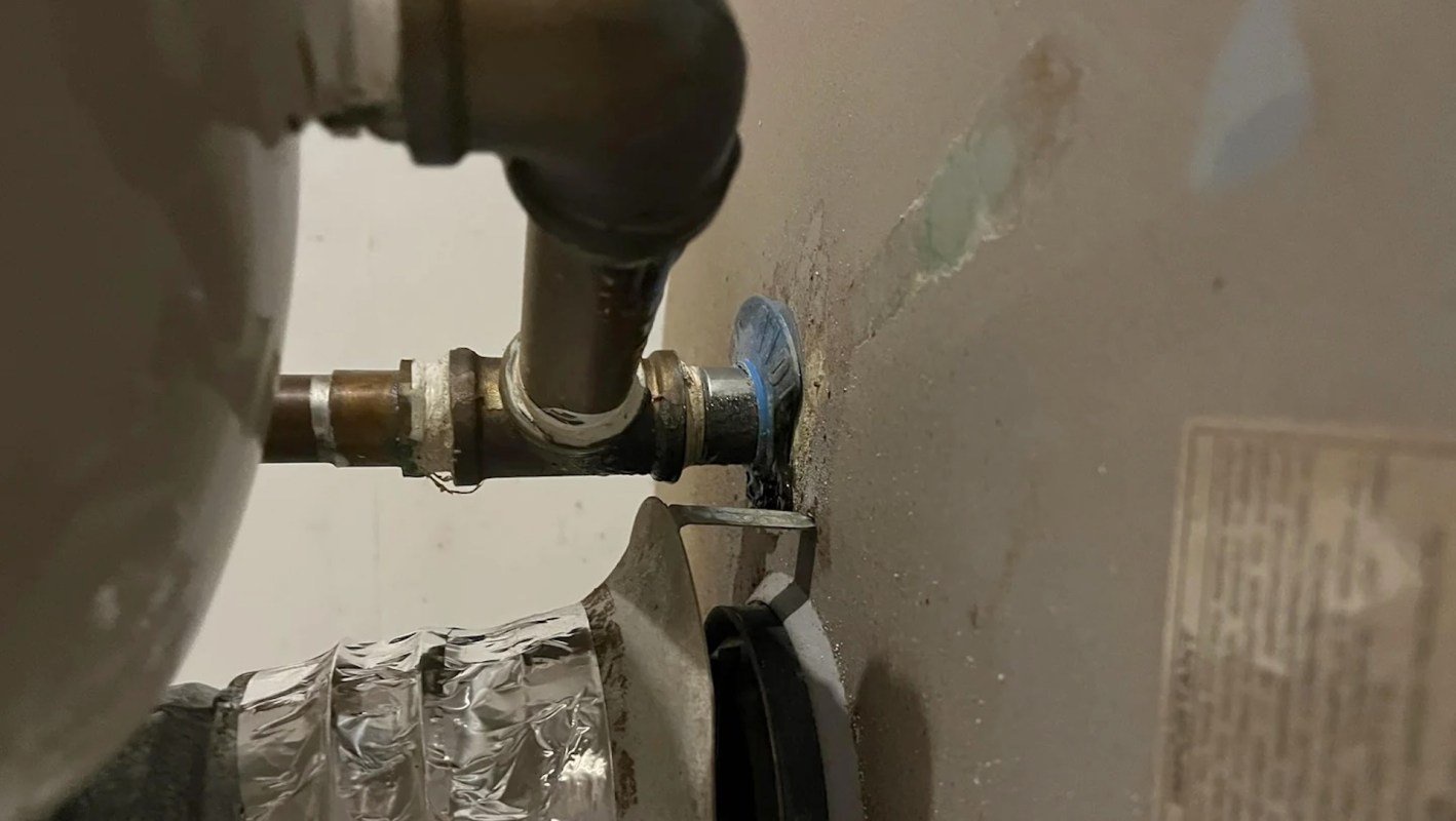 A metallic pipe connection on a water heater with a valve, showing a green stain from a blue plastic piece.