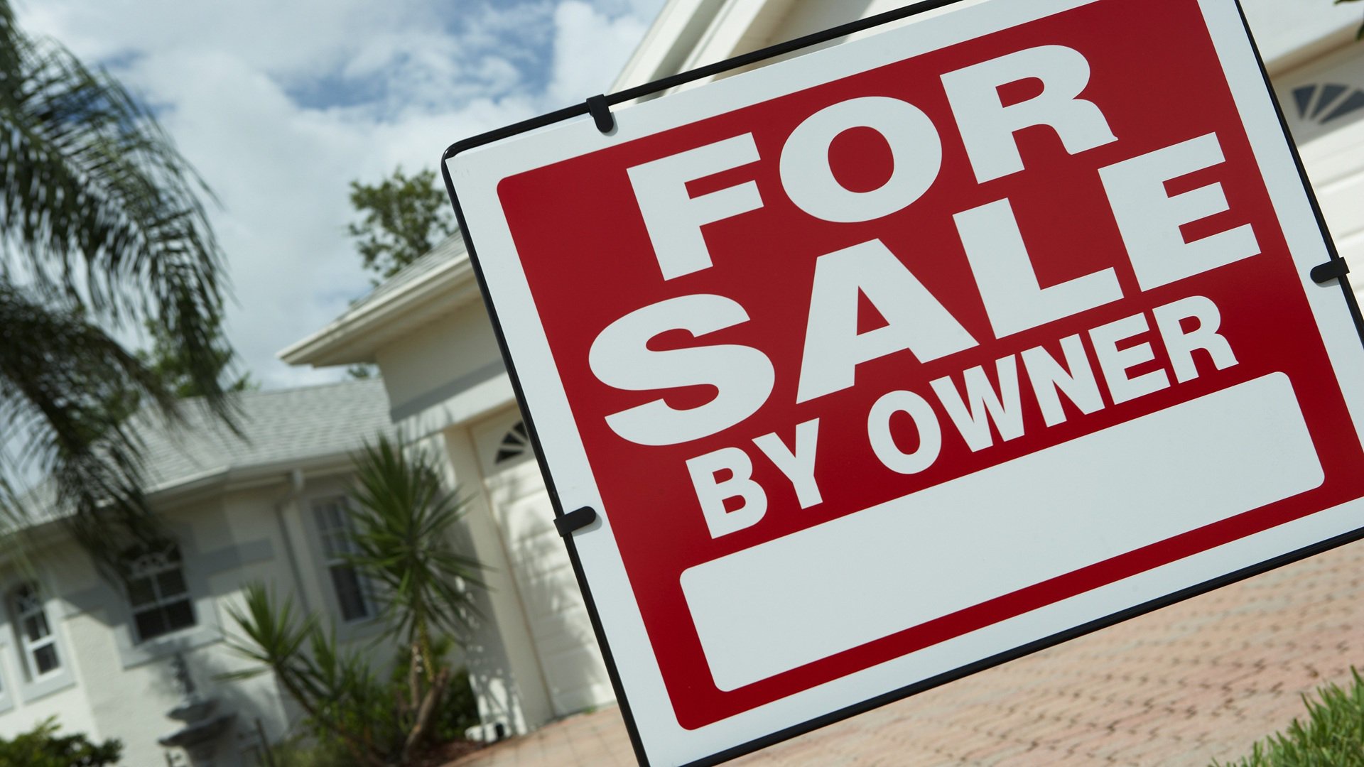 Discover a sign outside a house with palm trees and warm-weather plant life advertising a home for sale by owner