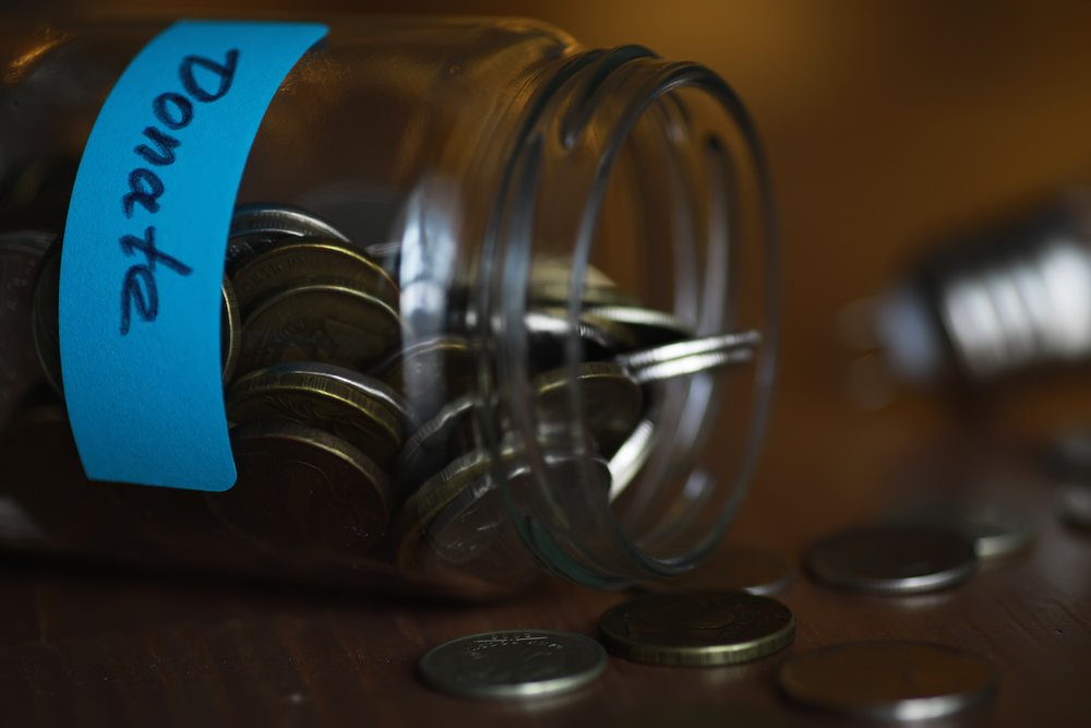Coins spilling from a jar with a blue label reading Donate