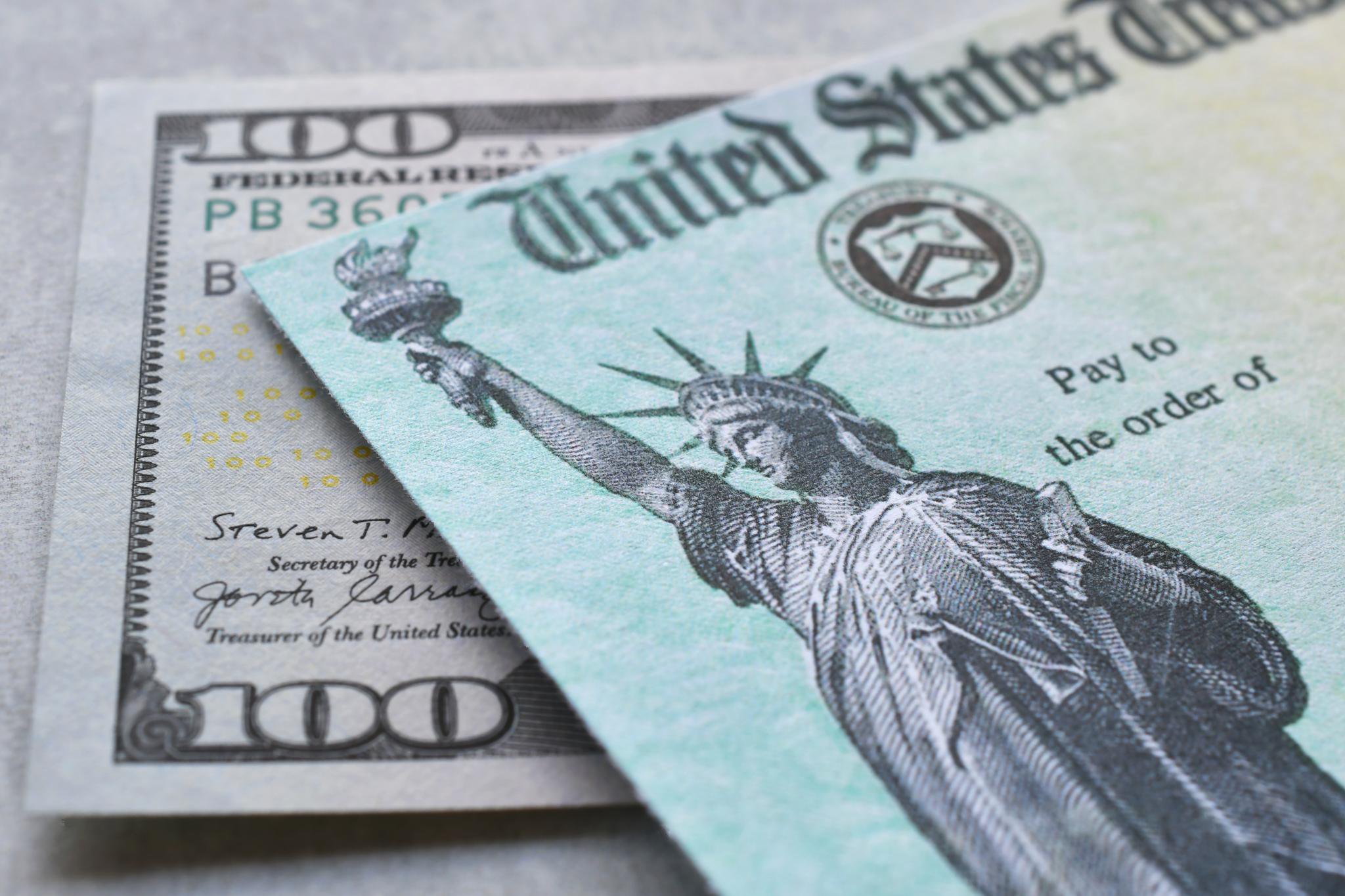 United States Government Treasury check resting on top of a hundred-dollar bill.