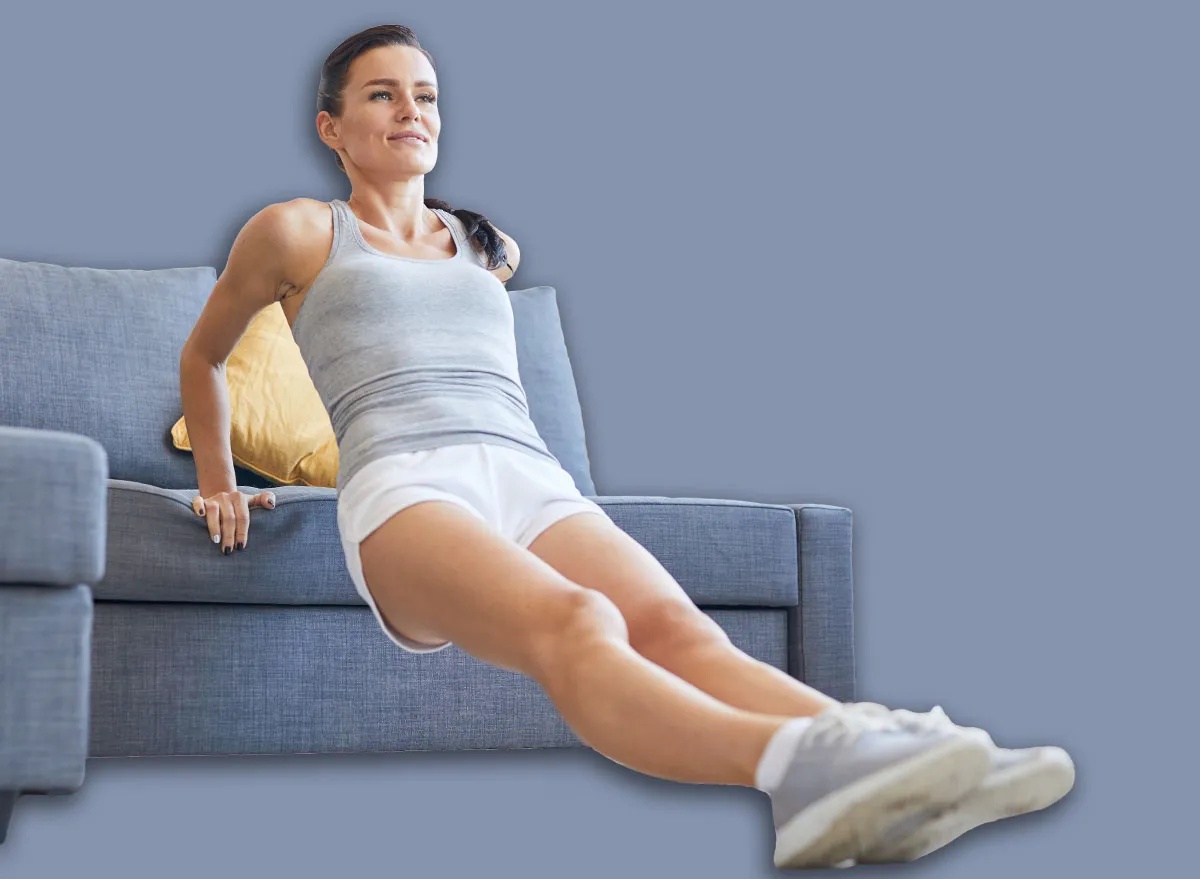 Young fit brunette woman in sportswear exercising by sofa in living-room