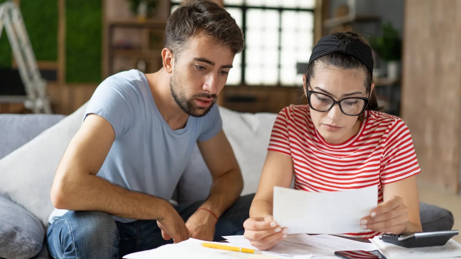 Getty Images A young man and woman sit together on the sofa looking at paperwork