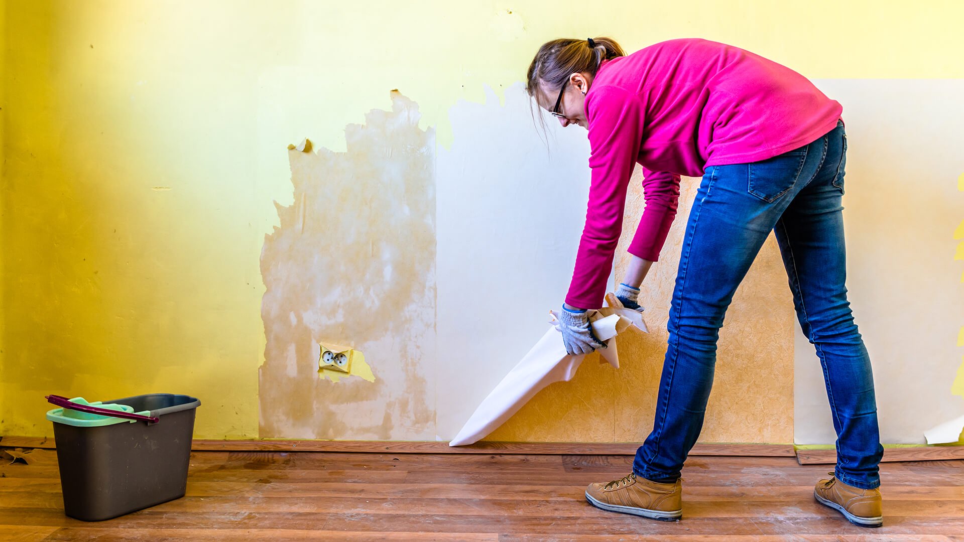 Discover a woman is making repairs to an interior wall of a home by ripping out wallpaper and renovating or painting