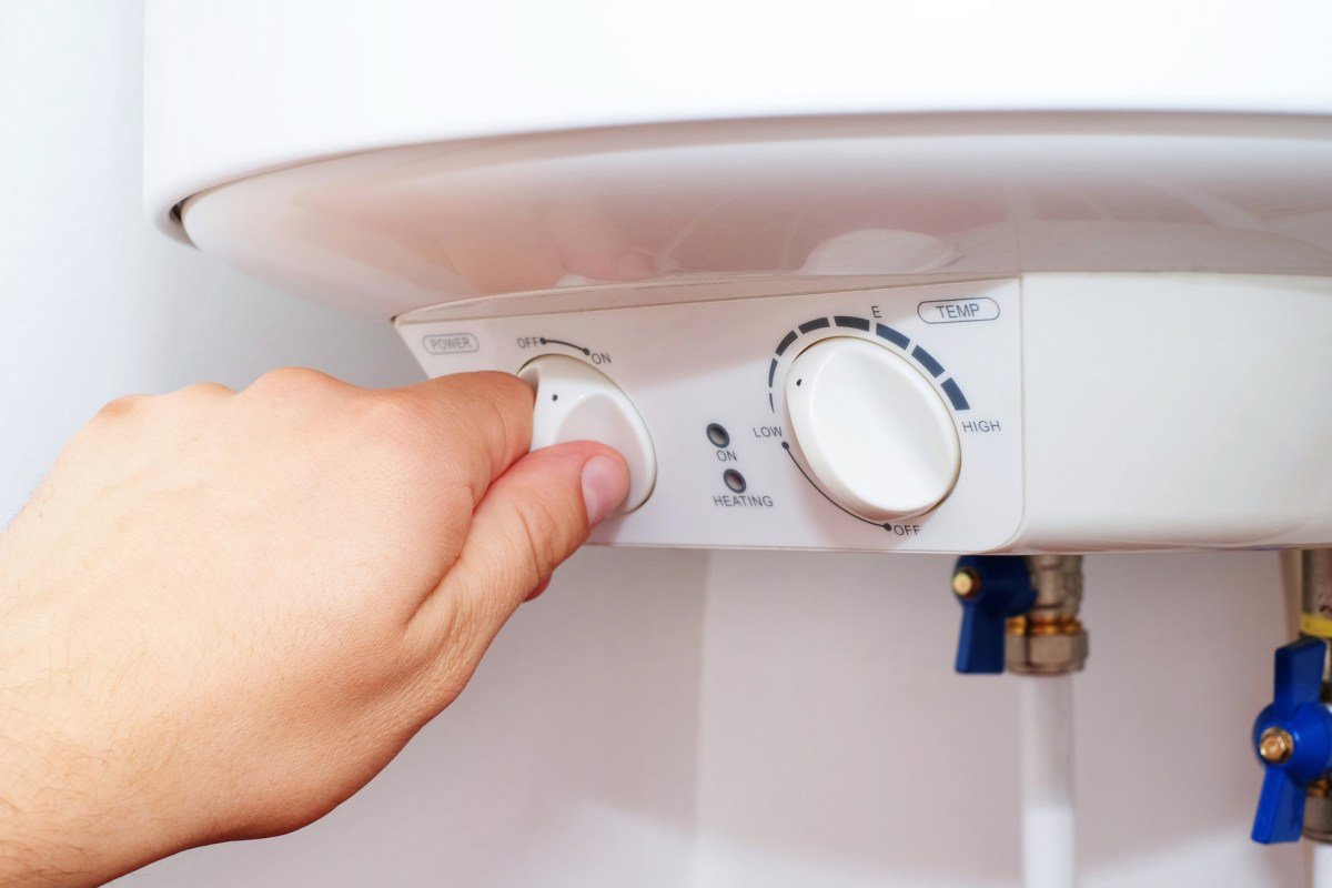 A hand adjusts the temperature and power settings on a water heater control panel.