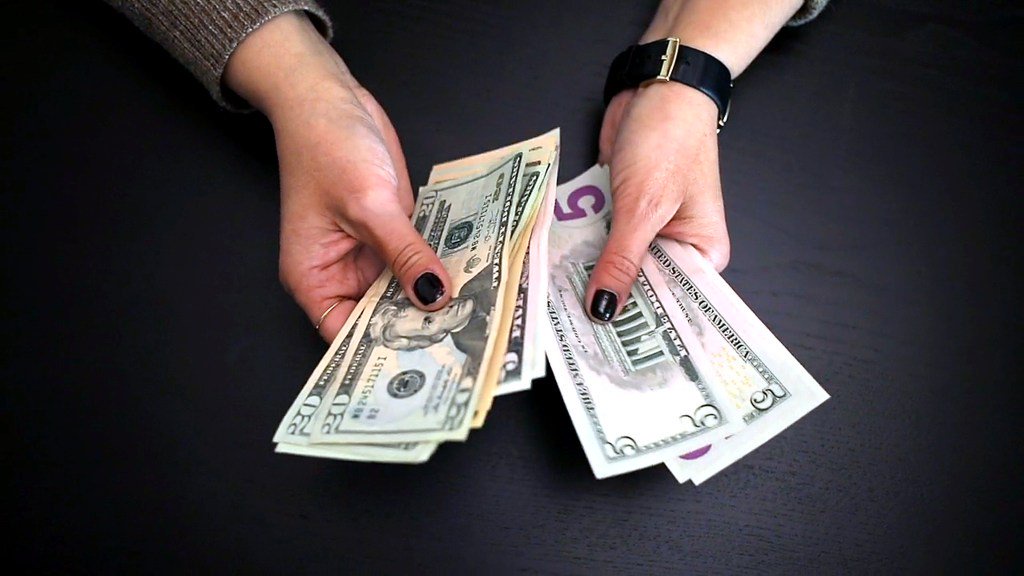A close-up of hands counting US dollar bills.