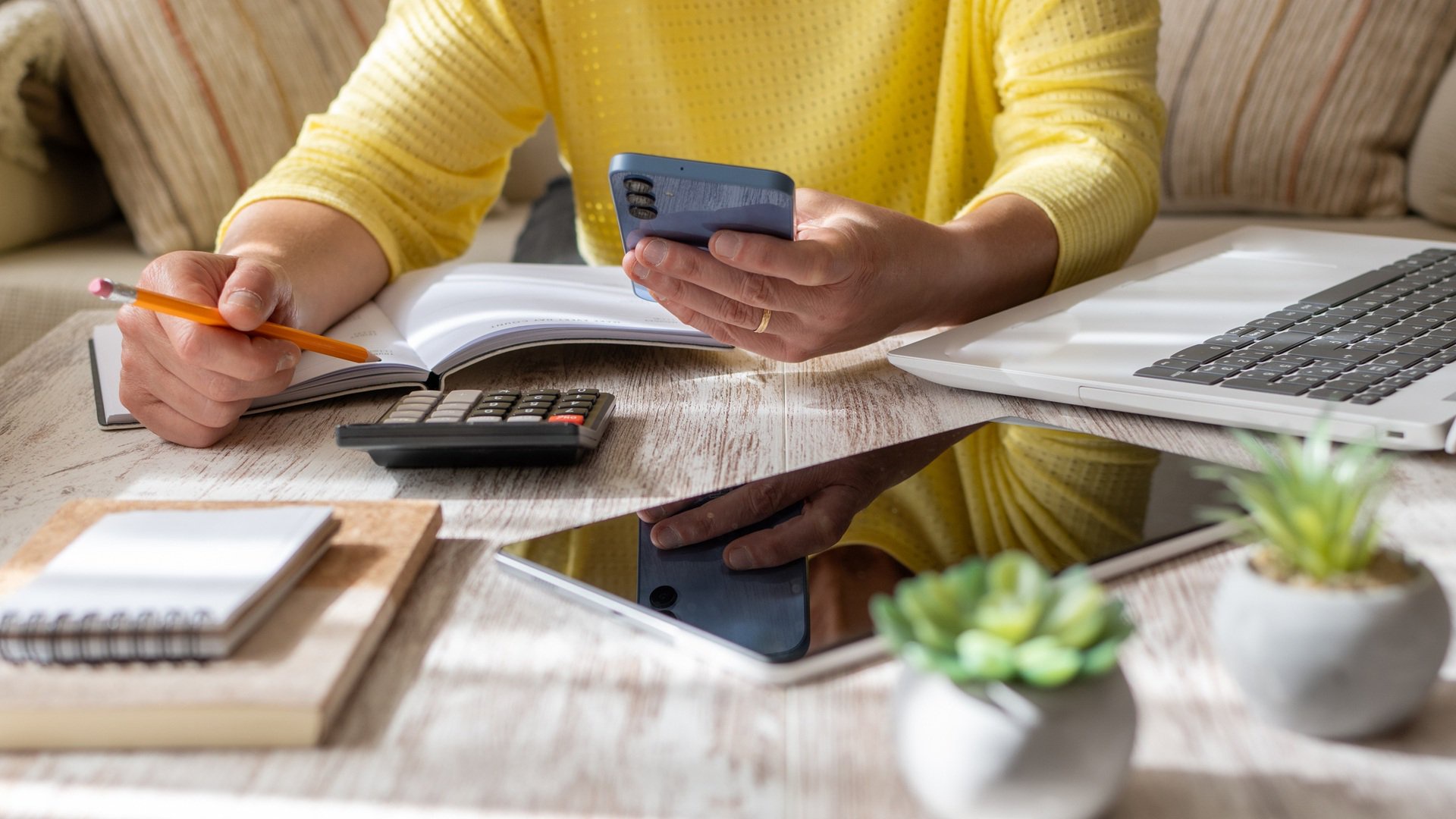 Discover a woman sitting on a couch, checking financial documents with calculator in hand inside her home.