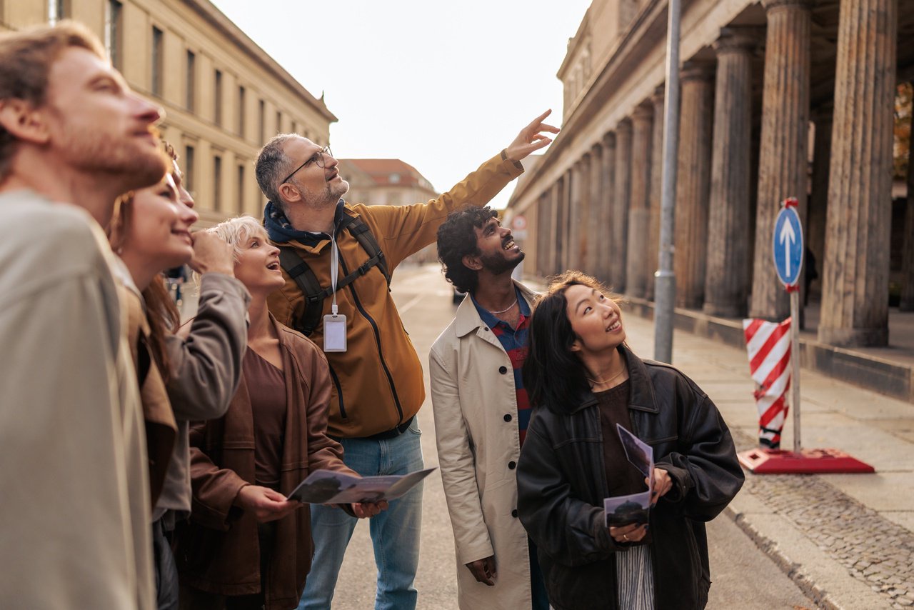 A tour guide gestures while speaking to a group of attentive tourists outside a historical building
