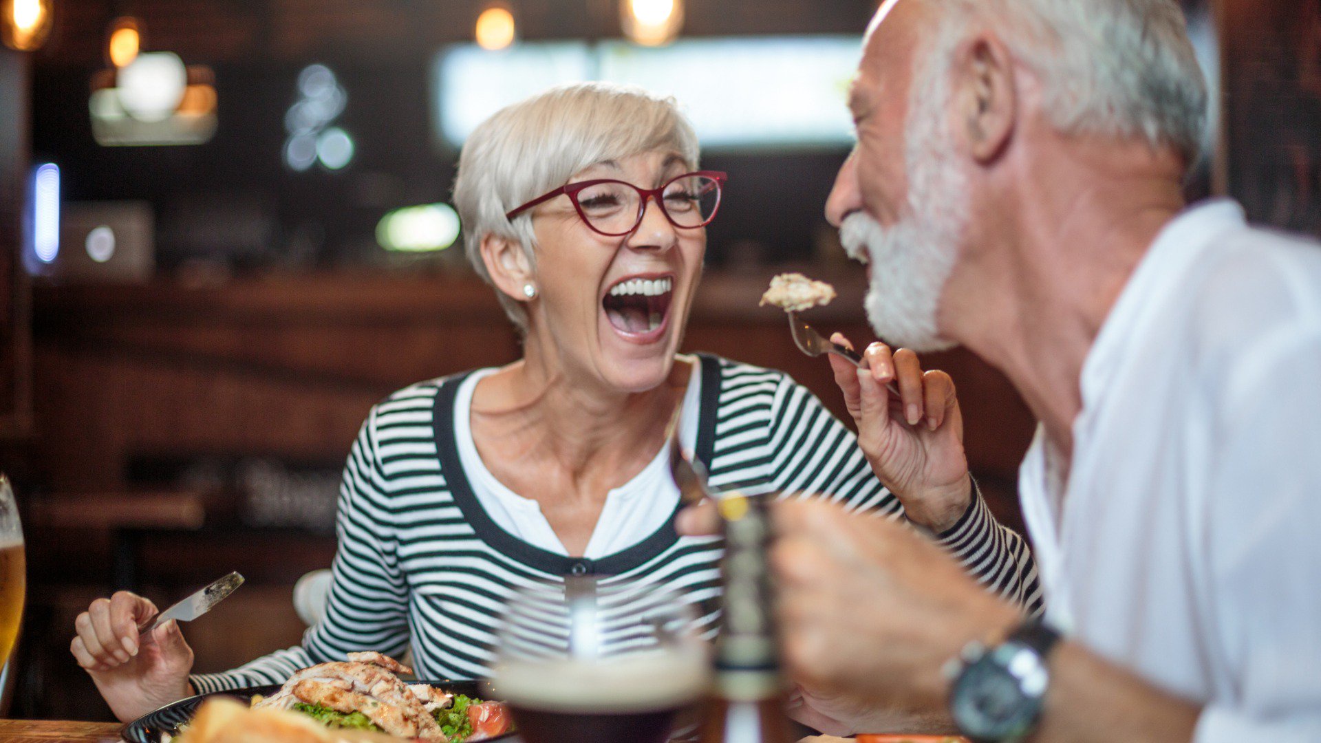 Discover a senior woman and man or couple laughing and smiling while having dinner at a restaurant.