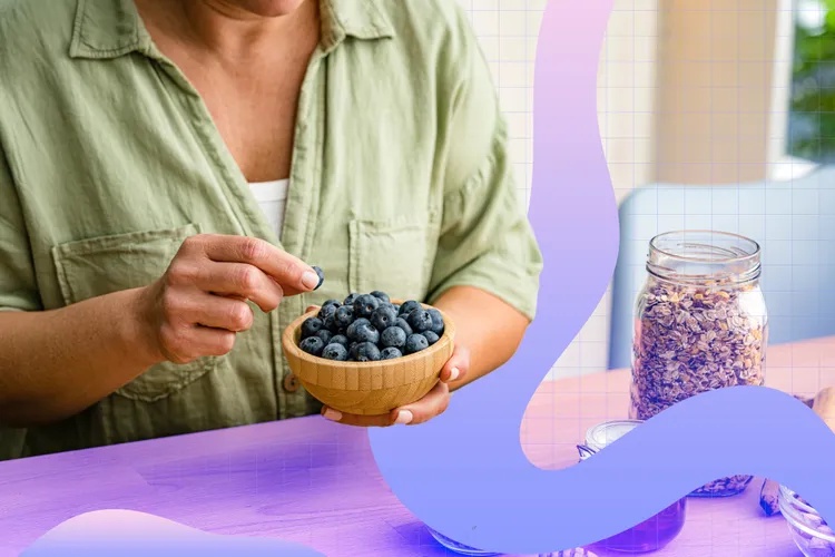 A person holding a wooden bowl of blueberries next to a jar of granola on a table