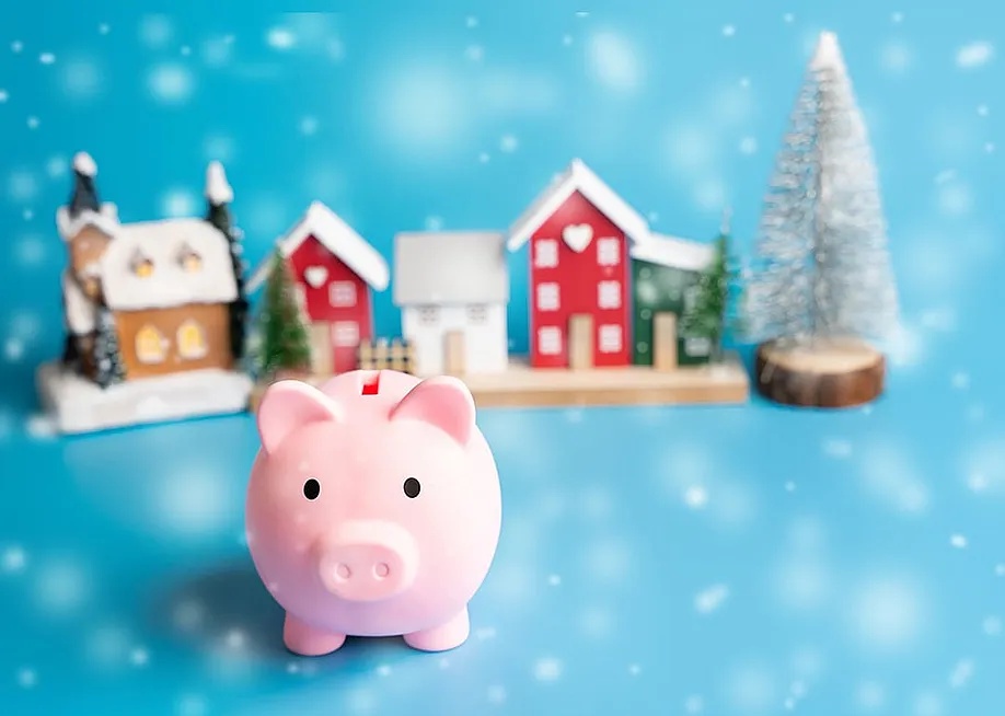 A figure of a piggy bank with Christmas houses and trees in the background as a concept of saving for the holiday season. — Andrii Yalanskyi // Shutterstock