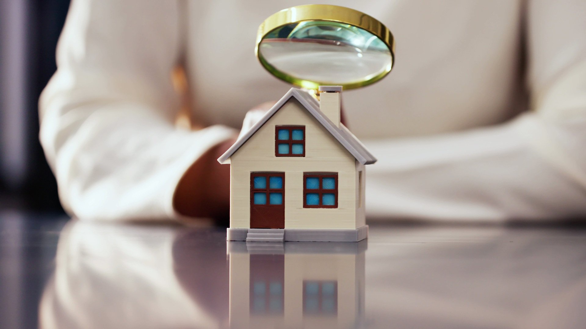 Discover a woman inspecting a miniature house with a magnifying glass, representing the details of buying a home