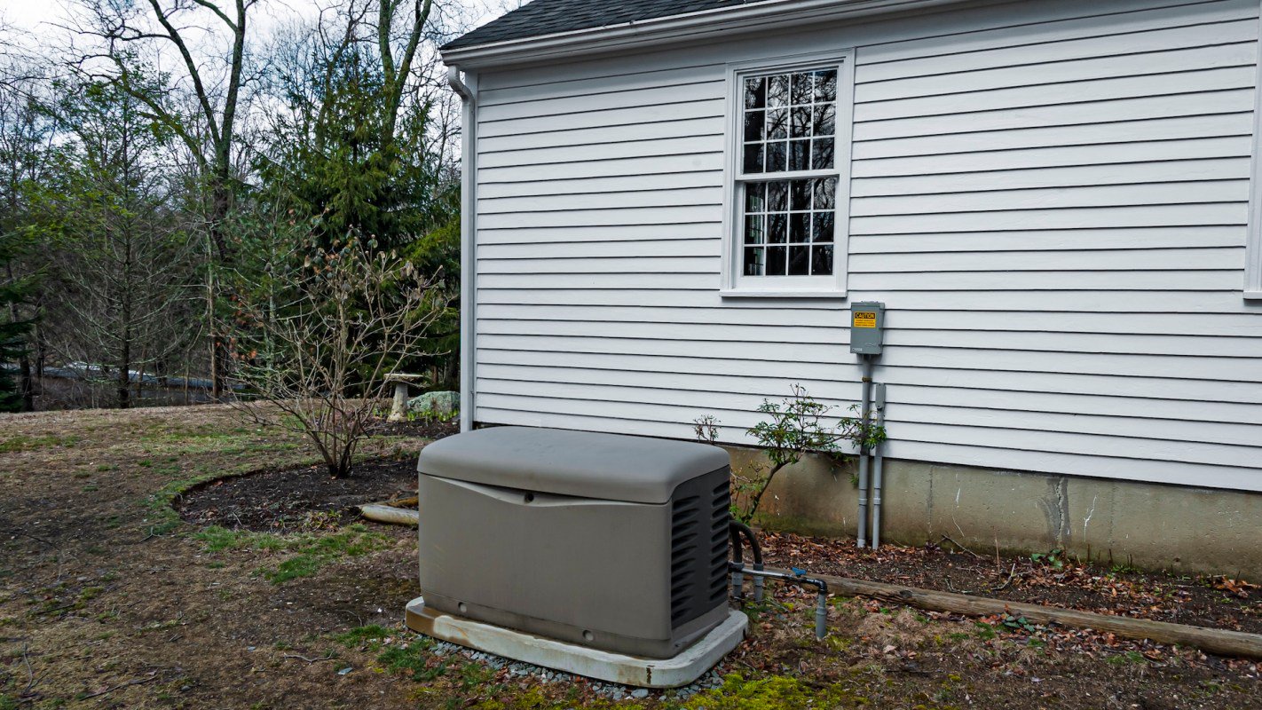 A generator placed next to the side of a house, with a window and electrical meter nearby.