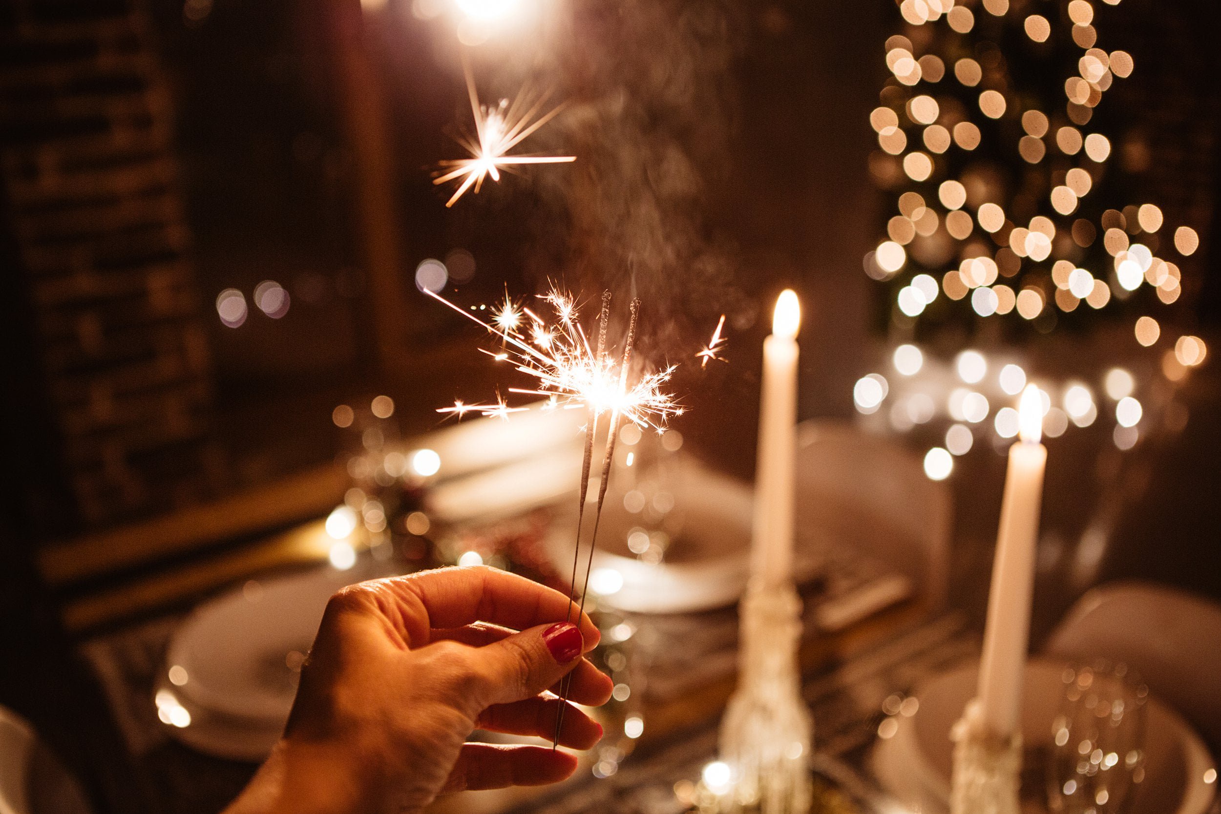 Hand holding a sparkler with candles in the background