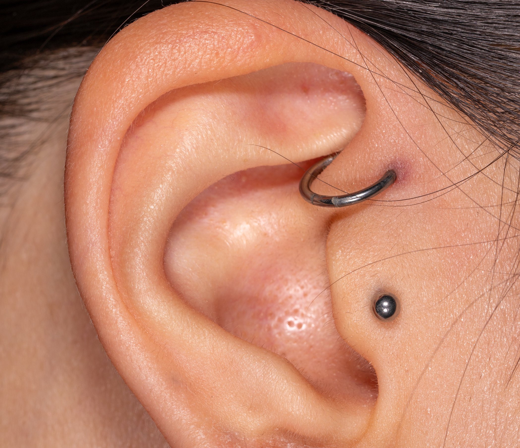 Close-up of an ear with a small hoop cartilage piercing and a black stud piercing on the earlobe