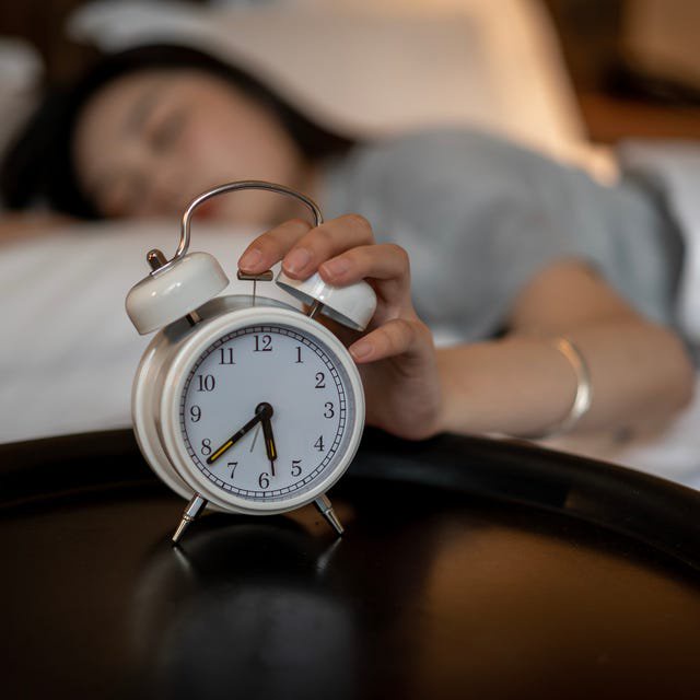 A young Asian woman presses her alarm clock in bed