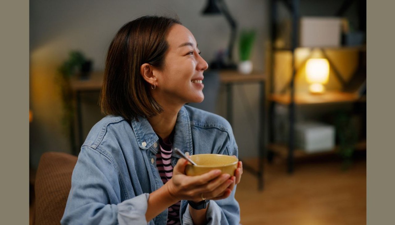 A woman smiles holding a warm bowl of healthy soup like that in the Fat Flush Soup Challenge