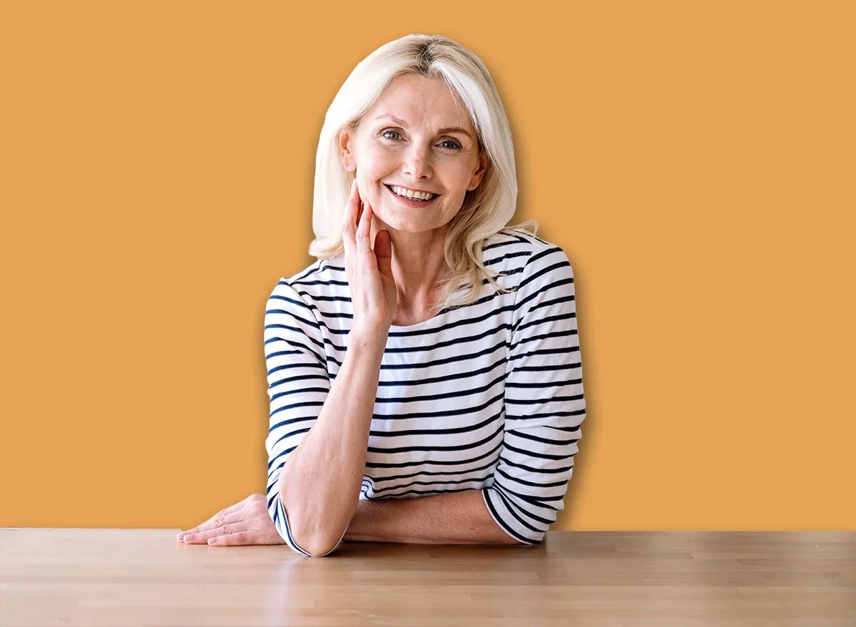 Cheerful middle aged woman standing near table at home kitchen, smile and looking at camera. Portrait of confident joyful female entrepreneur in casual clothes