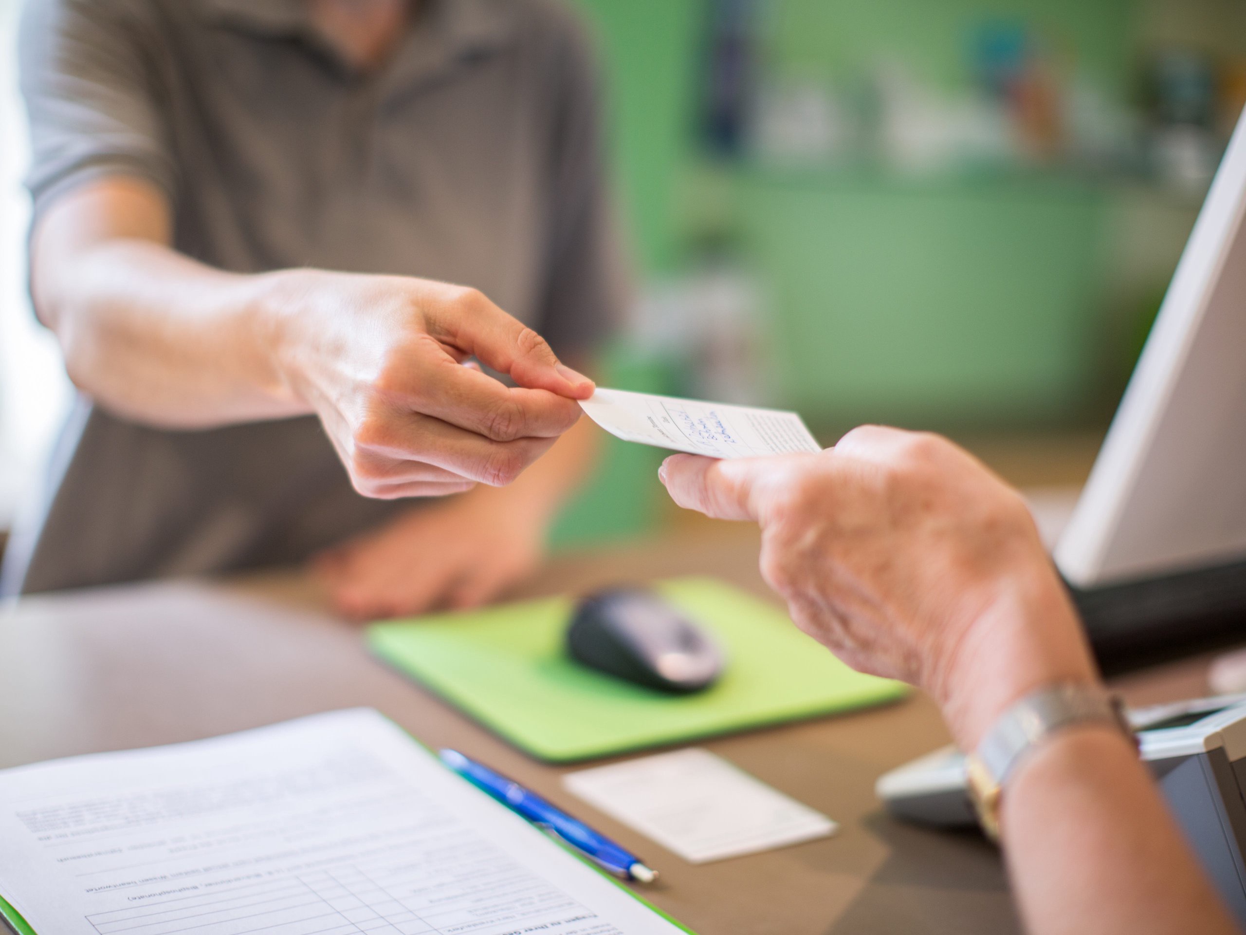 Close-up of a receptionist giving a health card to female patient at clinic. Focus on hands of female with a health card.