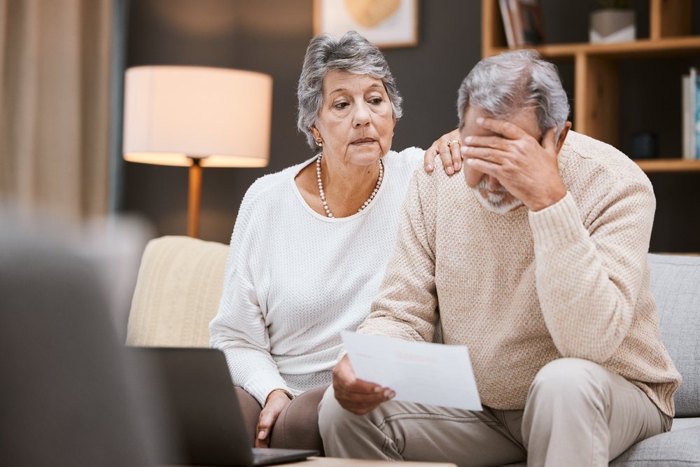 Worried older couple reading a letter beside an open laptop