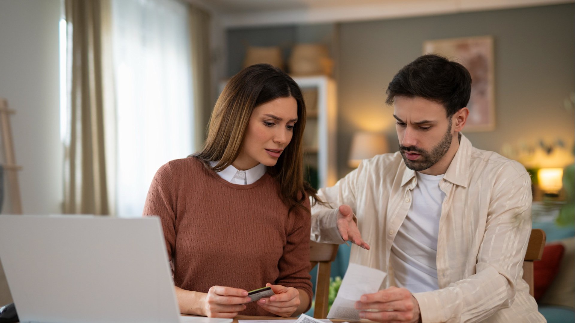 Discover a young couple looking worried as they manage their personal finances and budget with a laptop and documents