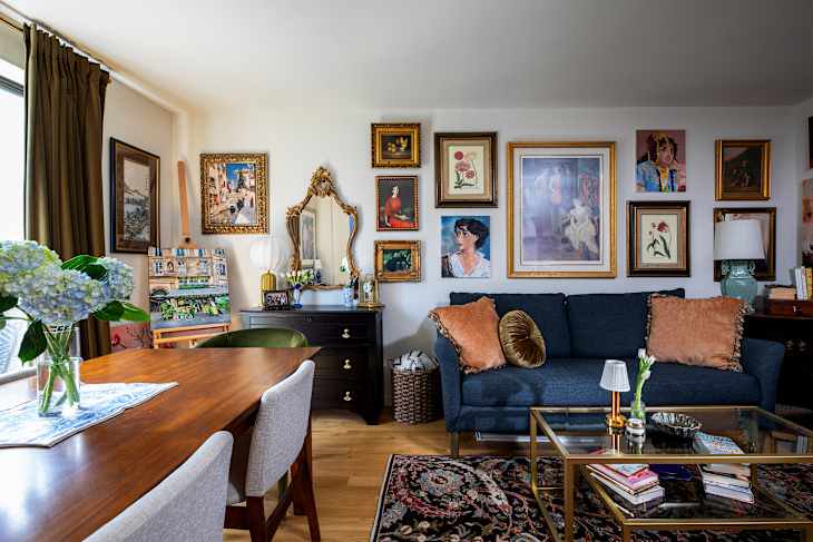 Cozy living room with a blue sofa, decorative pillows, a wooden dining table, and an art-filled wall.