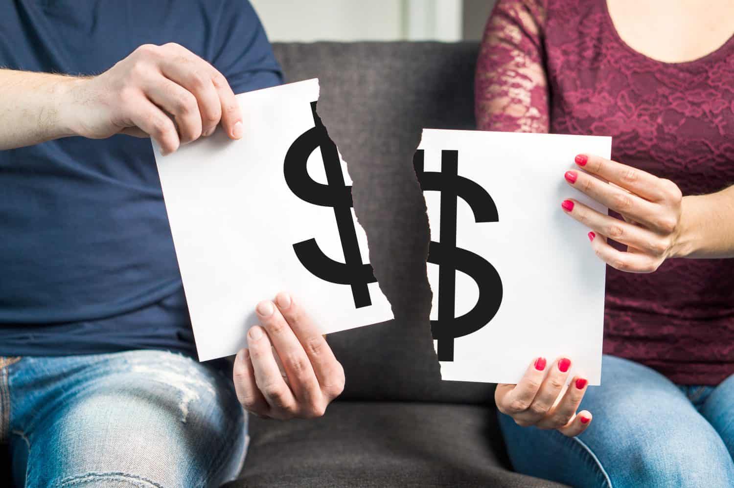 A man and a woman, seated, are each holding half of a white sheet of paper featuring a large, torn black dollar sign. The man, on the left, wears a blue shirt and jeans, while the woman, on the right, wears a maroon lace top, jeans, and has red nail polish.