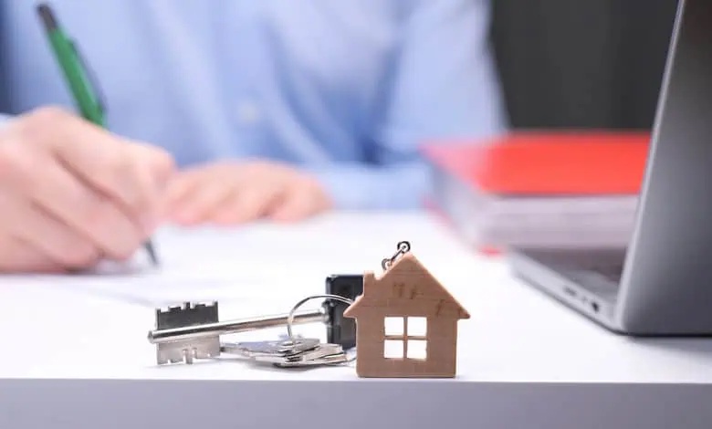A person is sitting at a desk, using a pen to write on a document. There is a key with a house-shaped keychain.