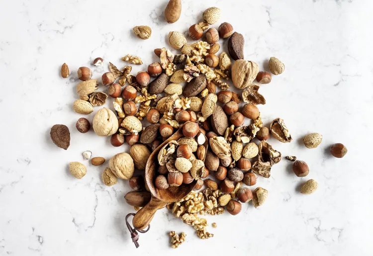 Assorted nuts and seeds scattered on a surface with a wooden spoon among them
