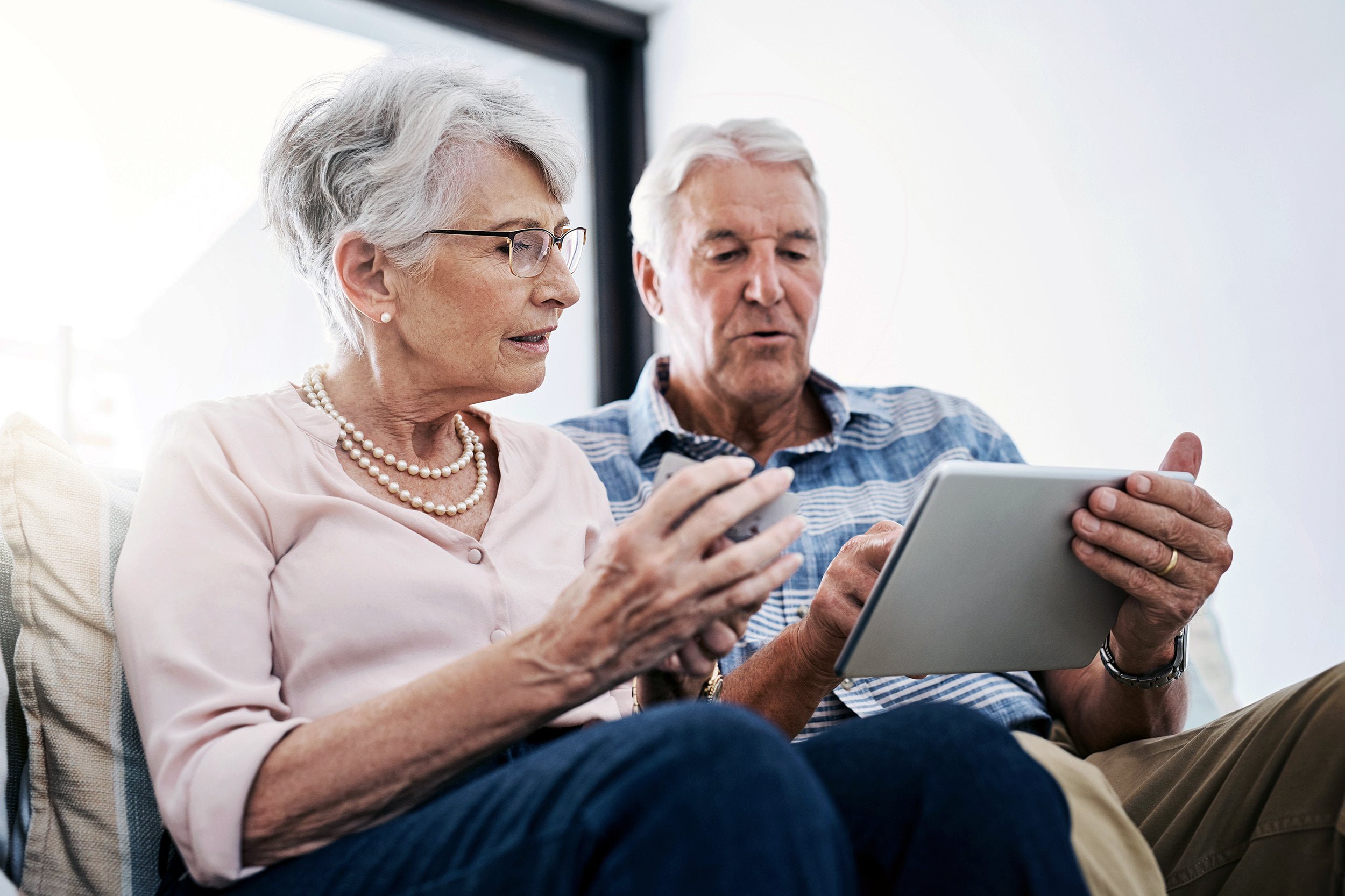 An older couple sitting together while looking at a tablet.
