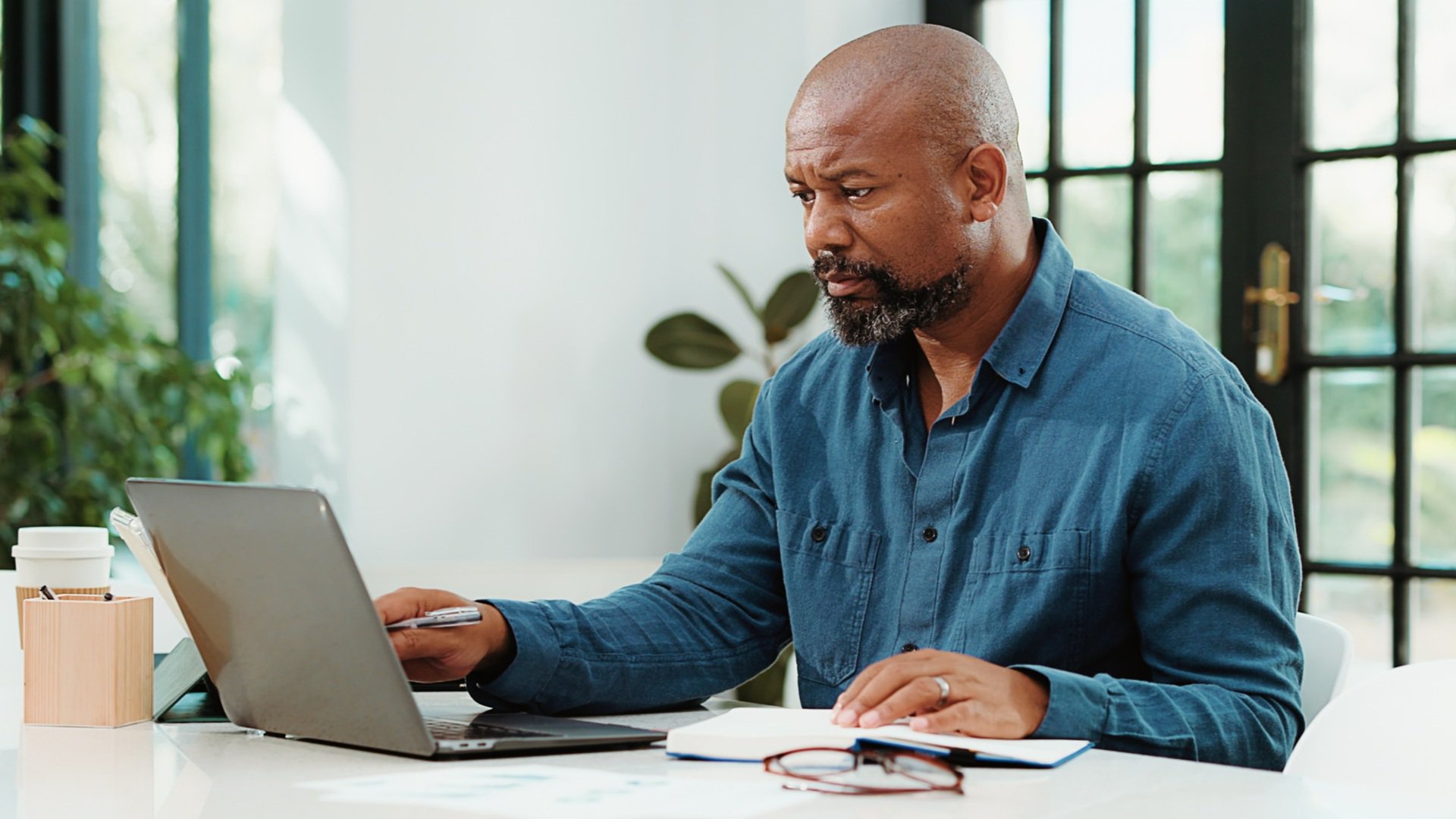 Discover a middle aged or mature man on his laptop computer sits at a desk reviewing documents
