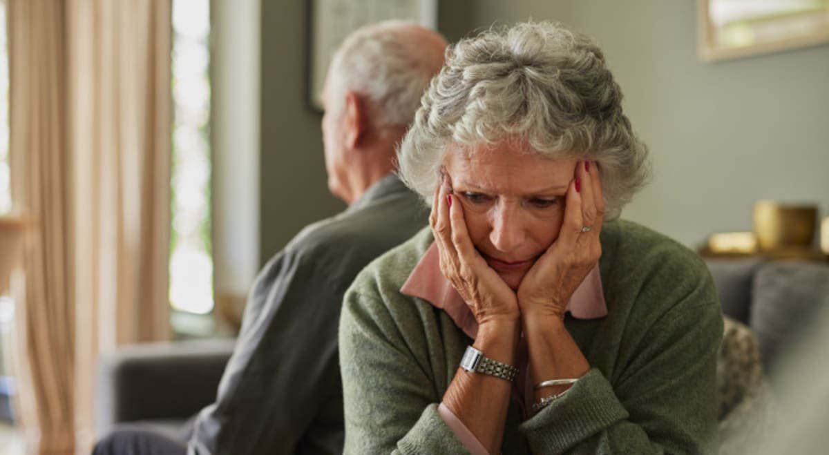 Upset senior couple sitting back to back on couch while looking away.
