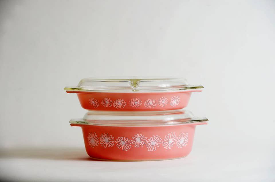 Stacked pink Pyrex dishes with a daisy pattern in white and a glass dish.