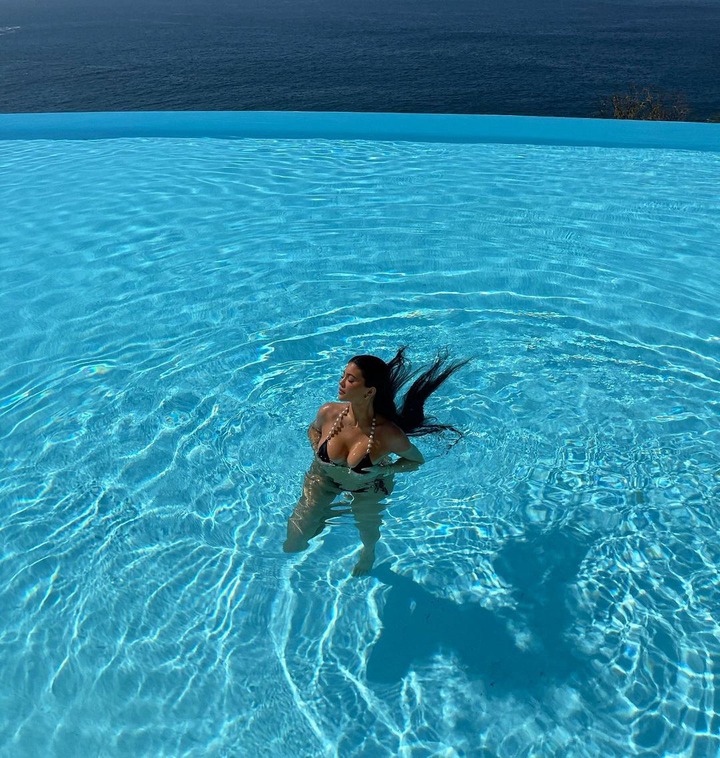 Bikini-clad, Kylie Jenner cups her ample cleavage as she poses inside a pool (Photos)