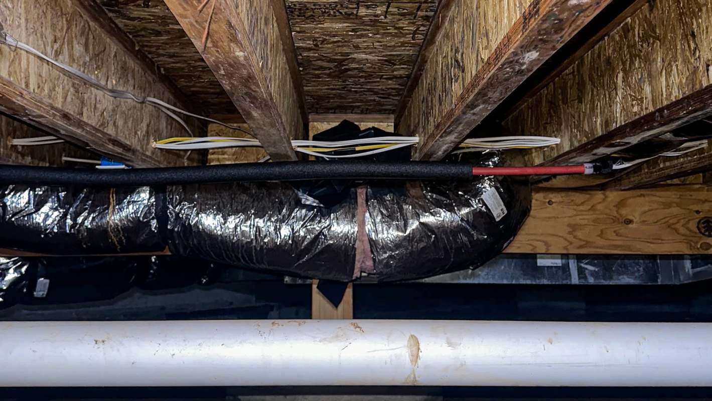 Exposed wooden beams and insulated ductwork in a crawlspace, with electrical wires visible overhead.