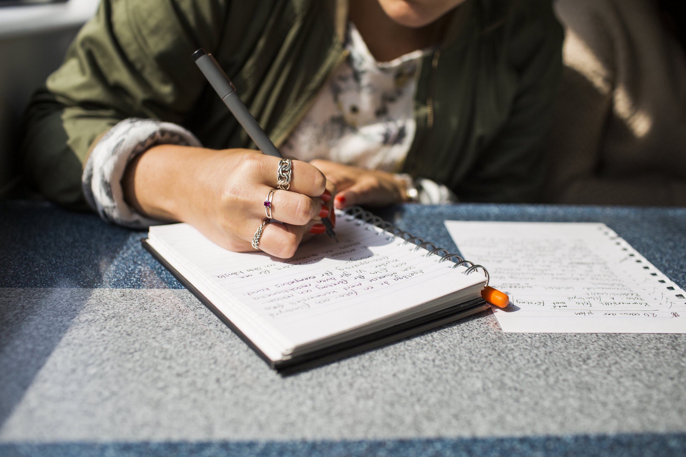 Person writing in a notebook on a train table, capturing travel thoughts