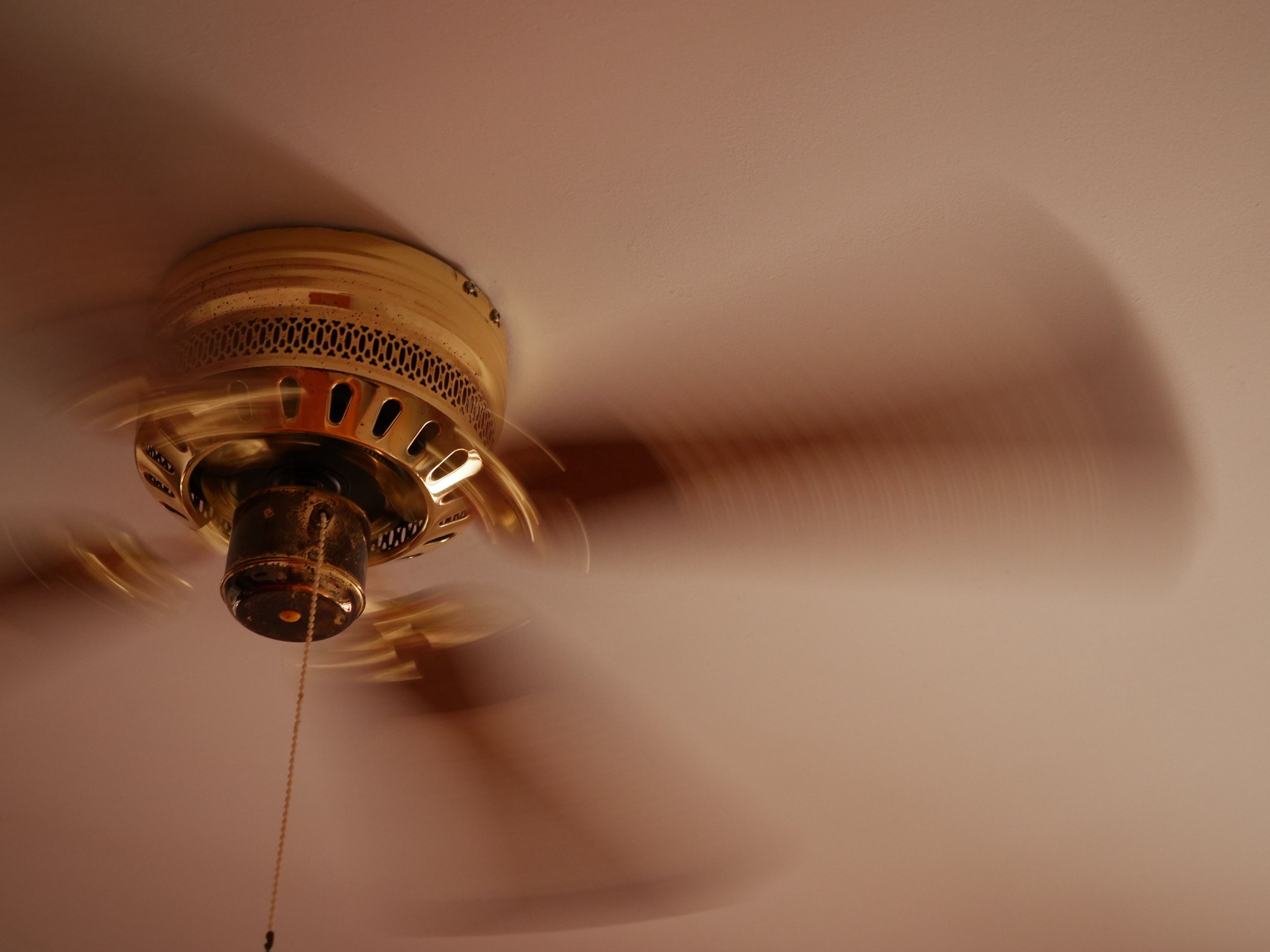Ceiling fan spinning at high speed, with its cord slightly blurred, indicating motion