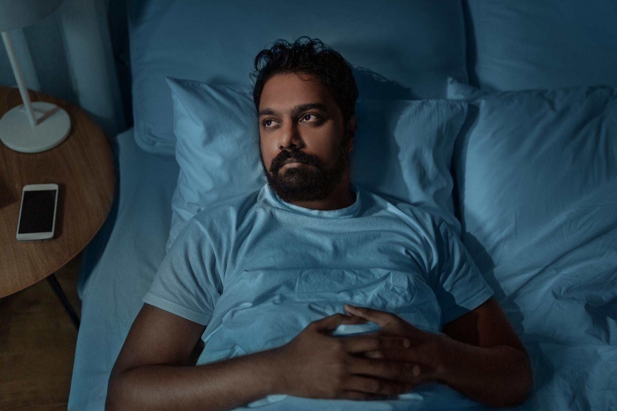An Indian man lying awake in bed at night, looking stressed and experiencing insomnia.