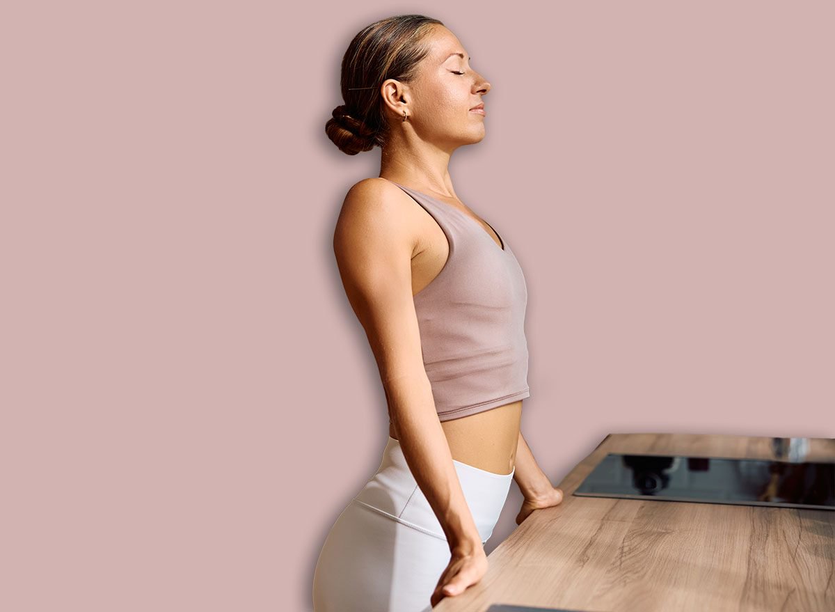 Athletic woman breathing with her eyes closed while enjoying in morning sun rays in the kitchen. Copy space.