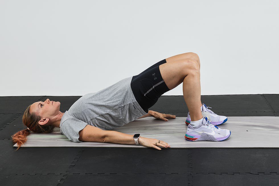 Person performing a bridge exercise on an exercise mat with a gray background.
