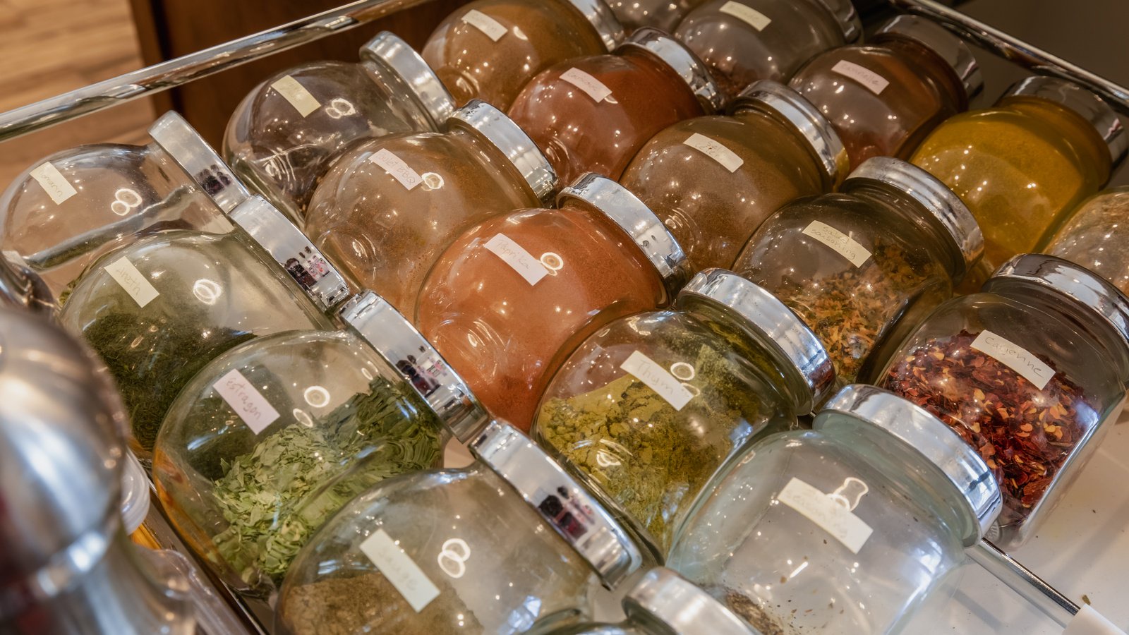 Rows of glass spice jars with written labels arranged in a drawer
