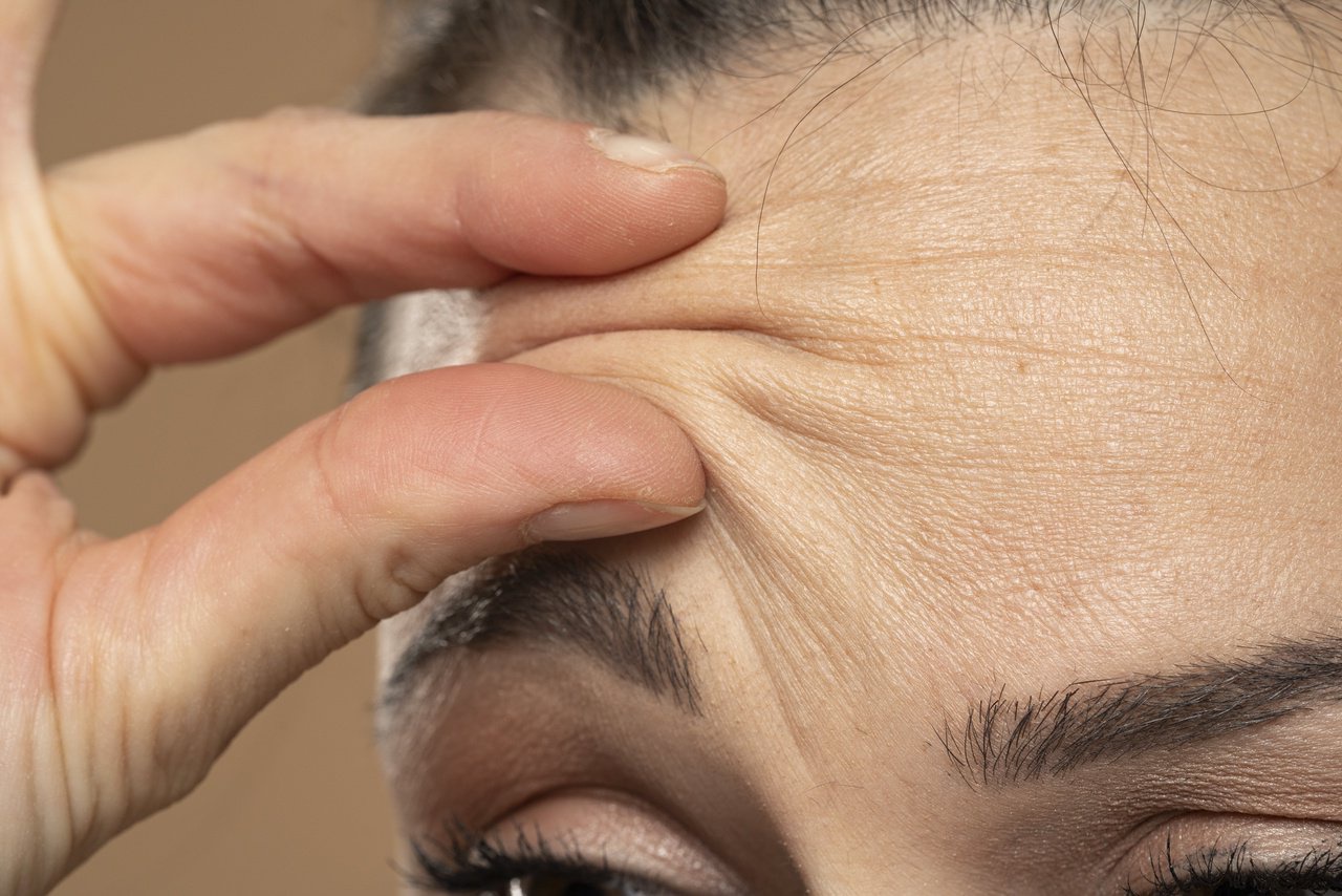 Close-up of a person pinching their forehead skin, highlighting wrinkles, possibly illustrating aging, skincare, or health-related content