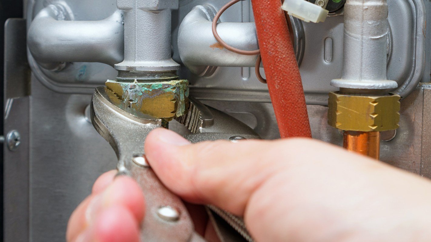 A hand using pliers to tighten a fitting on a metallic gas line.