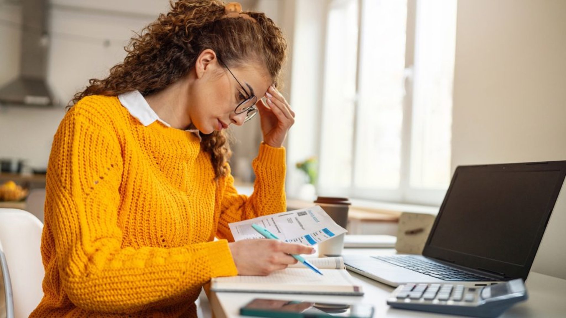 Discover a young, stressed woman looking over bills in her home, worried about her budget and overall finances.