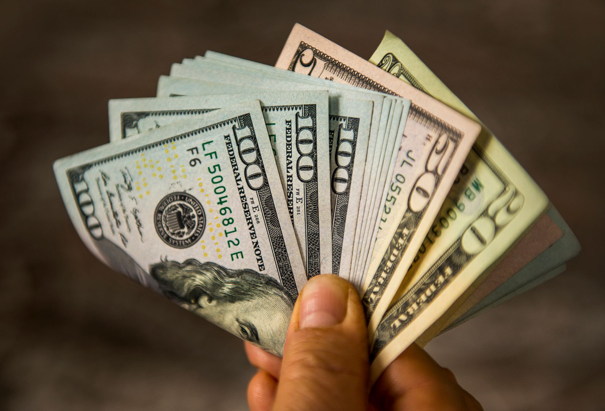 Hand holding a fanned stack of US dollar bills, including $100, $50 and $20 notes