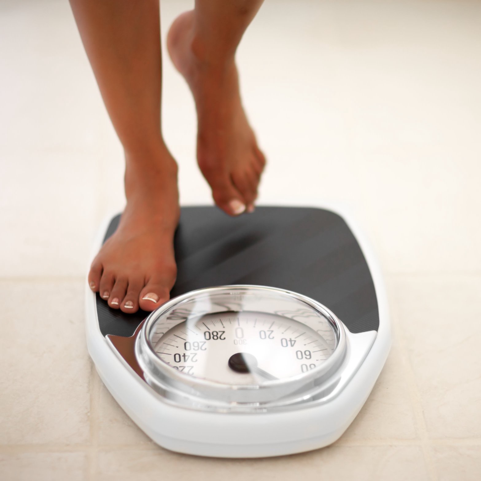 A person is stepping onto a bathroom scale, showing a focus on weight measurement